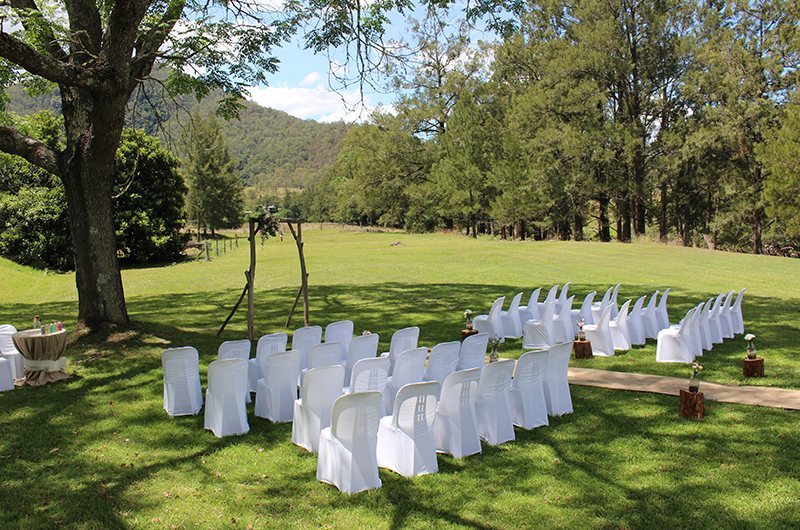 Wedding ceremony set on the resort lawn — white chairs facing an arbour under the mountains